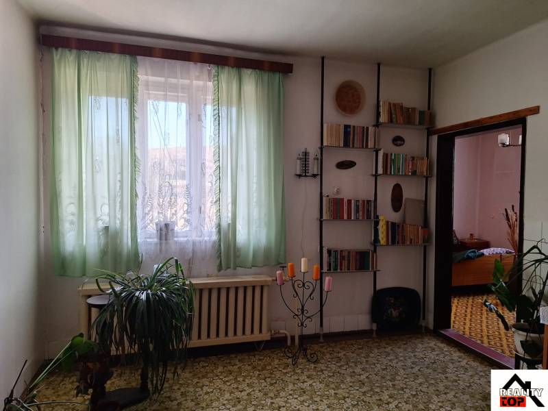 Ein Zimmer in einem Einfamilienhaus mit einem Bücherregal, grünen Vorhängen, Pflanzen und Kerzenhaltern.