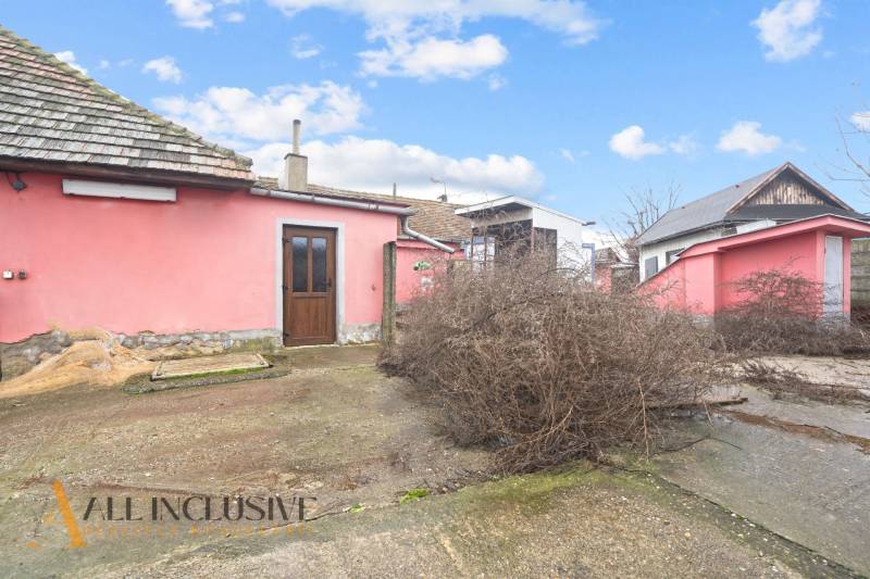 Ein Einfamilienhaus in Šintava mit rosa Fassade, ungepflegtem Hof und Holztüren.