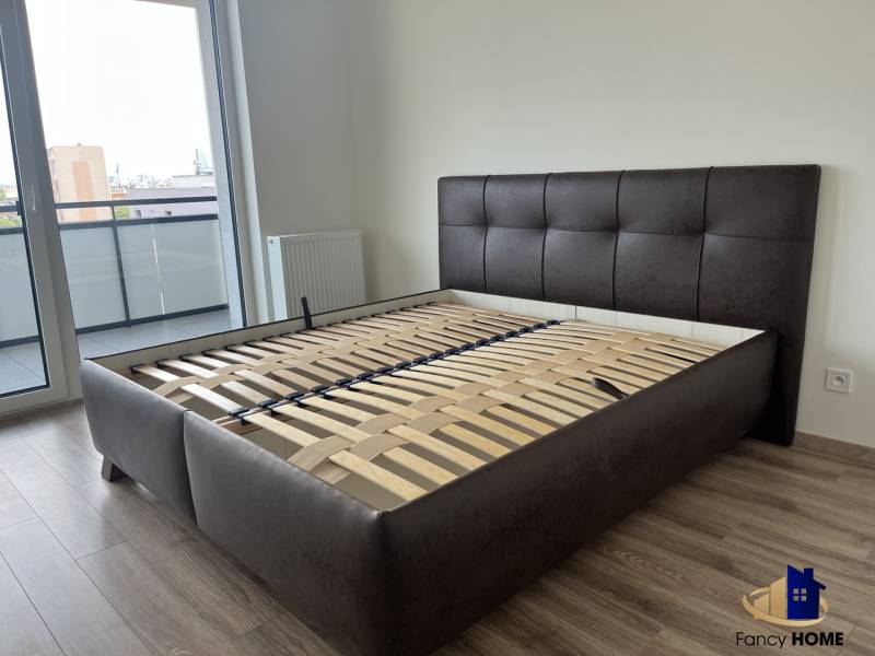 Schlafzimmer mit Bett ohne Matratze und Balkon in einer 2-Zimmer-Wohnung, Boden mit Holzdekor.
