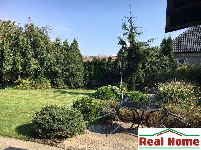 Der Garten des Einfamilienhauses in Čierna Voda mit Rasen, Bäumen und einer Außensitzgelegenheit.