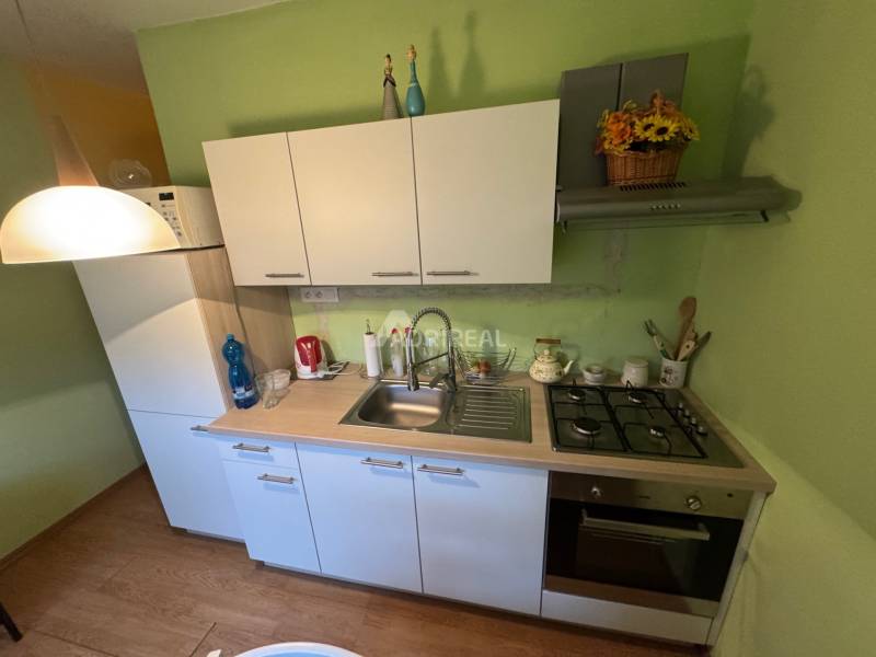 Küche in einer Einzimmerwohnung mit weißen Schränken und einem Boden in Holzoptik.