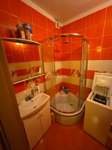Badezimmer in einer Einzimmerwohnung mit orangefarbenen Fliesen, Duschkabine und Waschbecken.