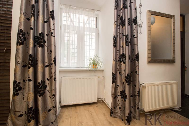 Ein Zimmer in einer 2-Zimmer-Wohnung mit einem Holzboden, Vorhängen und einer Pflanze auf der Fensterbank.