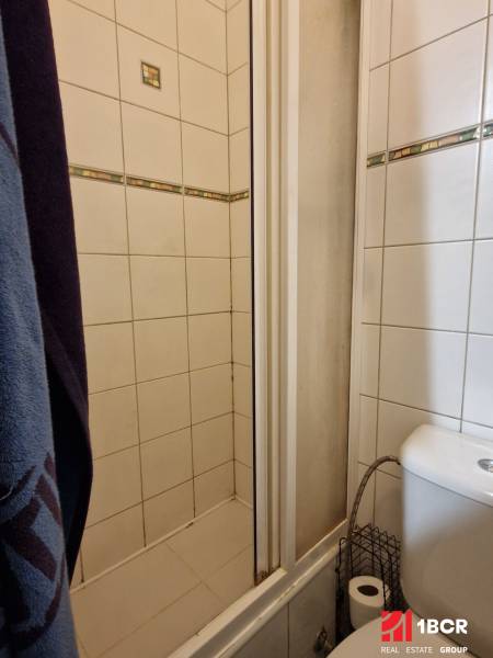 Badezimmer in einem Studio-Apartment mit Duschkabine und Toilette, gefliest mit weißen Fliesen.