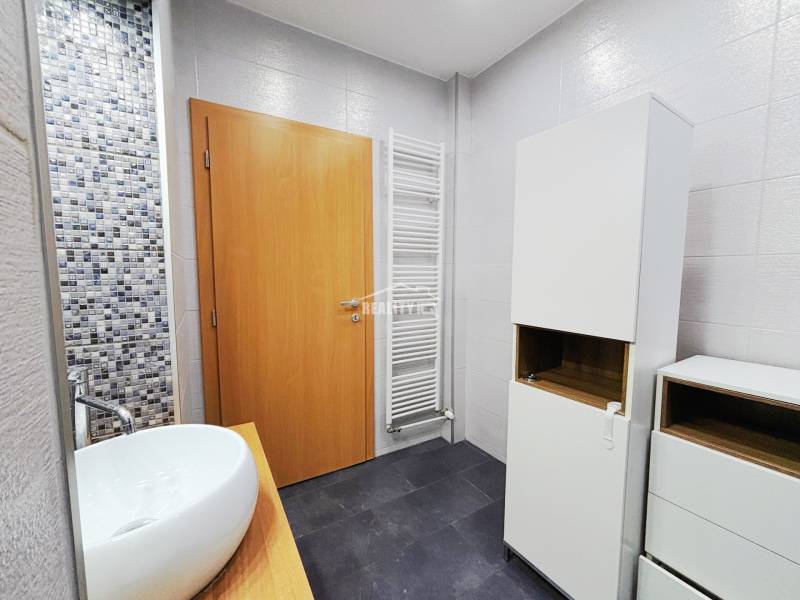 Badezimmer mit Waschbecken, weißen Schränken und Mosaikfliesen in einer 2-Zimmer-Wohnung.