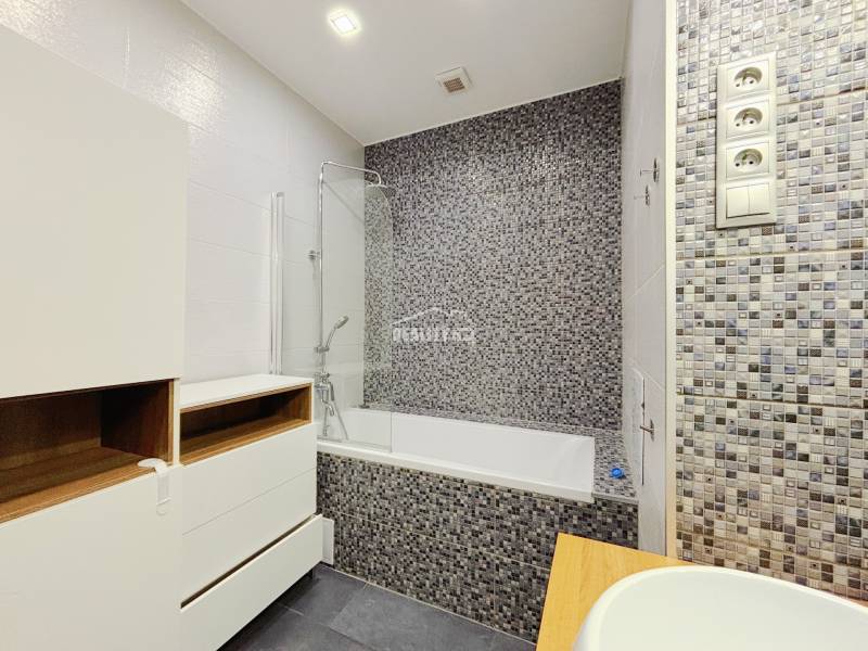 Badezimmer in einer 2-Zimmer-Wohnung mit Badewanne, Mosaikfliesen und Stauraum.