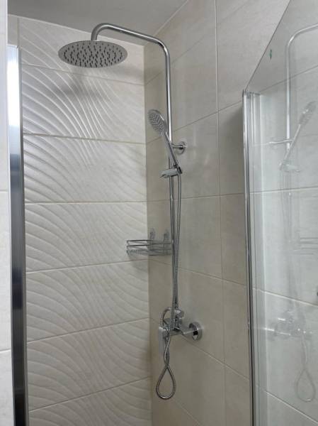 Duschkabine in einer Einzimmerwohnung, Verkleidung mit Textur und Glaswand.