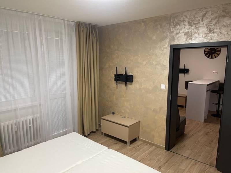 Innenraum einer Einzimmerwohnung mit Holzboden, Bett und Vorhängen am Fenster.