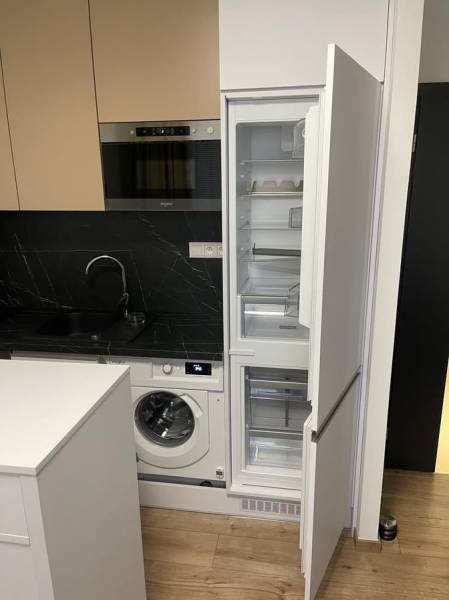 Küche in einer Einzimmerwohnung mit Waschmaschine, Holzboden und offenem Kühlschrank.