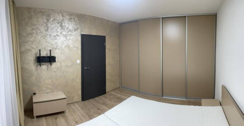 Schlafzimmer in einer Einzimmerwohnung mit Holzboden, Einbauschrank und TV-Halterung.