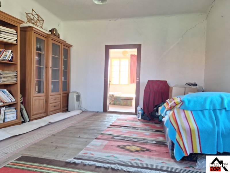 Ein Zimmer in einem Einfamilienhaus mit Bücherregalen, einem Bett mit einer bunten Decke und einem Teppich.