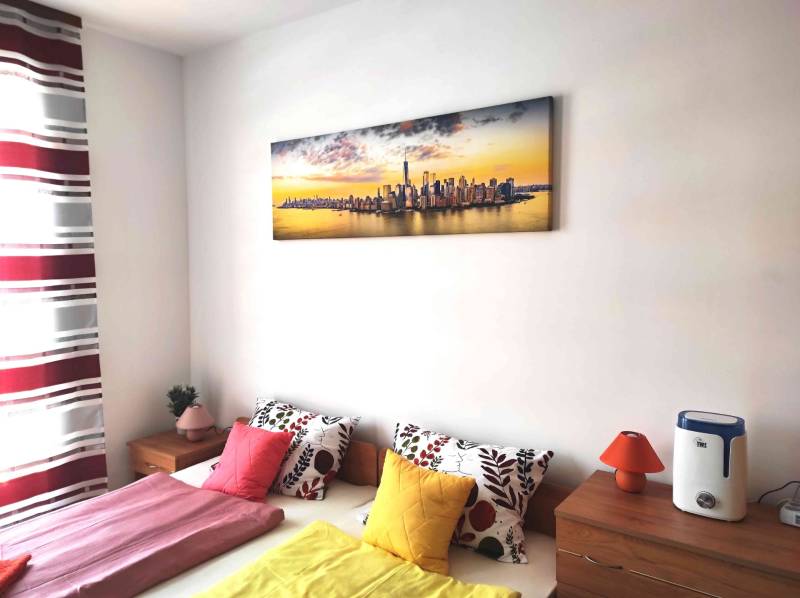 Schlafzimmer in einer Ferienwohnung mit bunten Kissen und einem Panorama-Bild.