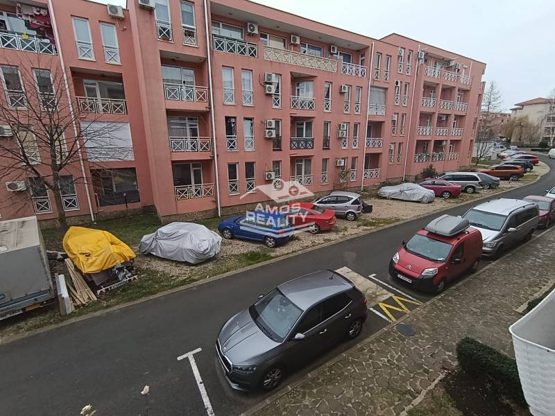Ferienwohnung in Burgas mit geparkten Autos vor einem rosa Gebäude.