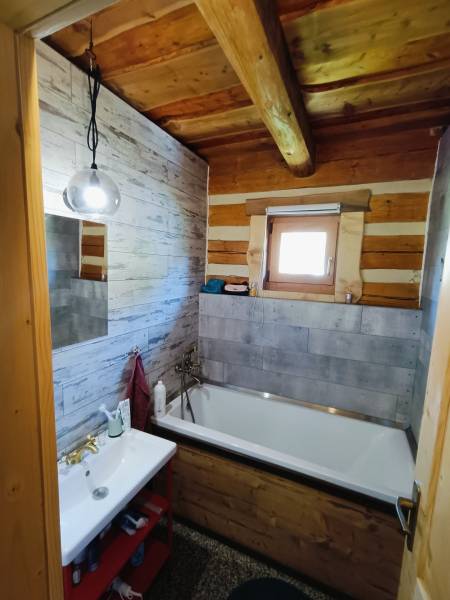 Ein Badezimmer in einer Hütte mit einer Badewanne, einem Waschbecken, Holzwänden und einer einfachen Lampe.