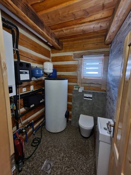Ein Badezimmer in einer Hütte mit Toilette, Waschbecken und technischen Geräten. Das Interieur wird von Holz dominiert.