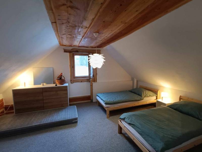 Dachboden der Hütte mit zwei Betten und einer Kommode mit Holzdekor.