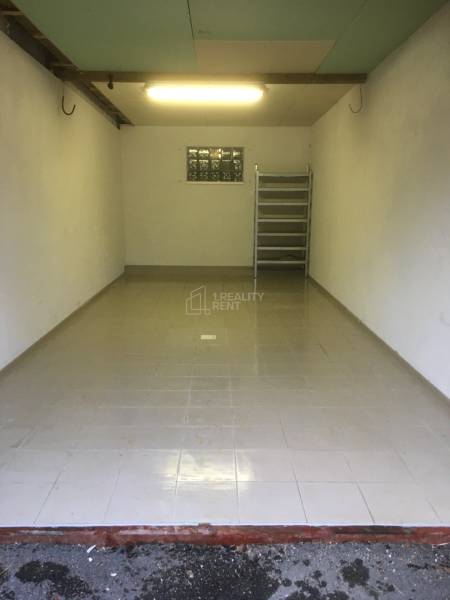 Ein Blick in eine leere Garage mit grauen Fliesen auf dem Boden und einem Regal im Hintergrund.