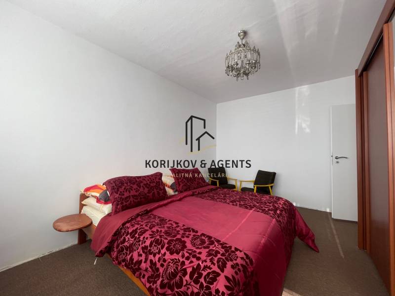 Schlafzimmer mit einem Bett mit gemusterten Bezügen, Deckenleuchte und Kleiderschrank in einer 3-Zimmer-Wohnung.