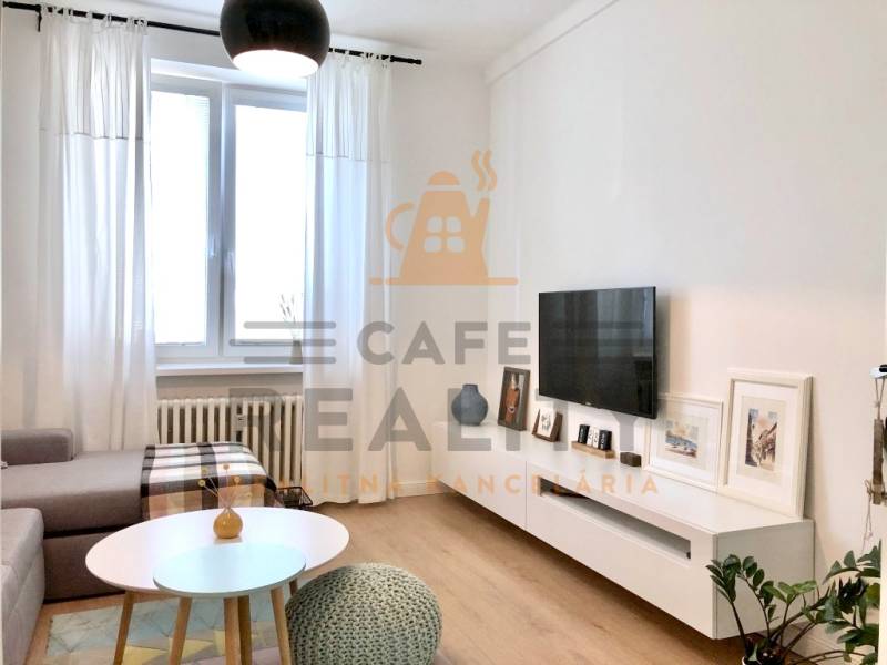 Wohnzimmer in einer Zweizimmerwohnung mit Fernseher, Sofa und Holzboden.