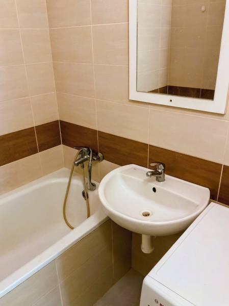 Badezimmer mit Badewanne, Waschbecken und Waschmaschine in einer 3-Zimmer-Wohnung, helle Fliesen.