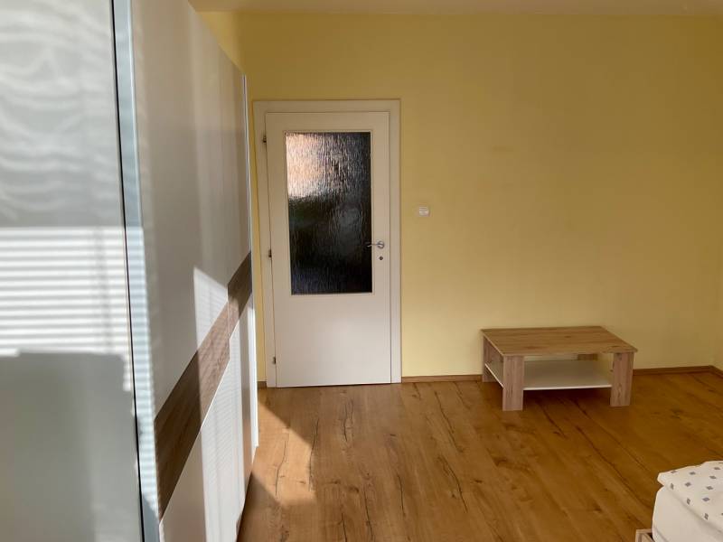 Ein Zimmer mit einem Holzboden, hellen Wänden und einfacher Einrichtung in einer 3-Zimmer-Wohnung.