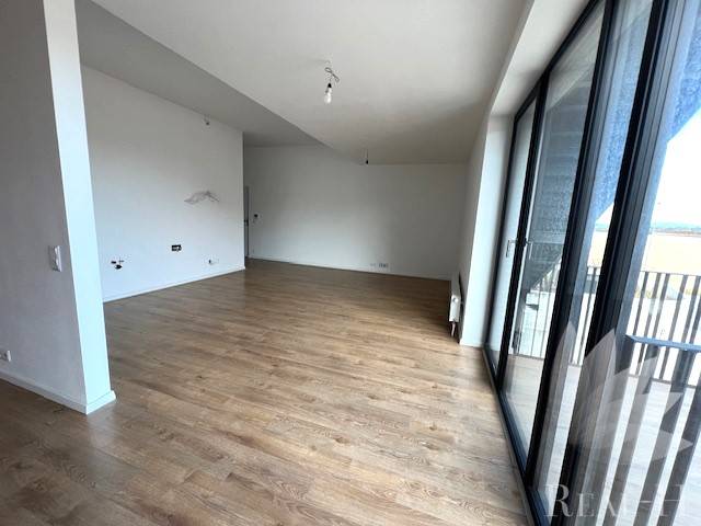 Geräumiges Wohnzimmer mit Holzboden in einer Zweizimmerwohnung mit Glastüren zum Balkon.