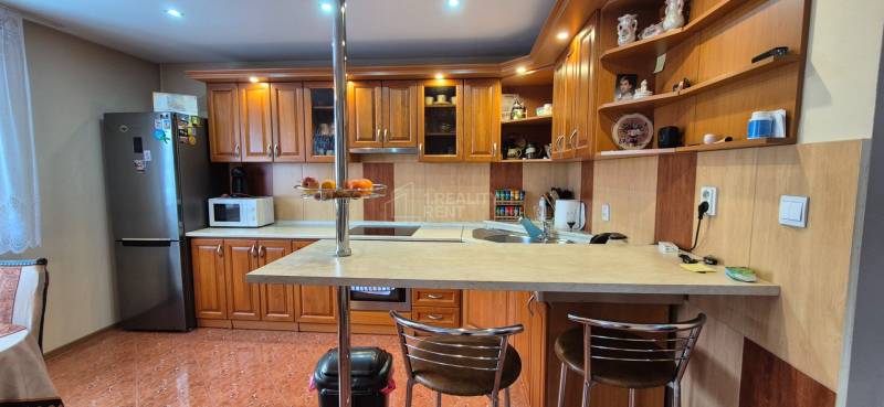 Küche in einem Einfamilienhaus mit Holzschränken, Bartresen und Geräten.