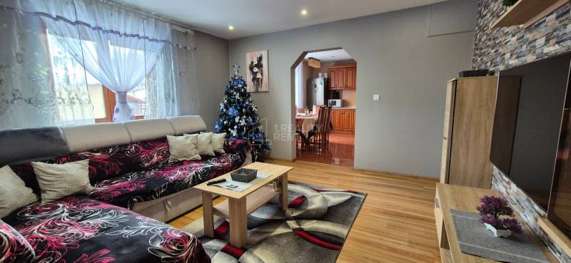 Im Wohnzimmer eines Einfamilienhauses gibt es ein Sofa, einen Weihnachtsbaum und einen Boden mit Holzdekor.