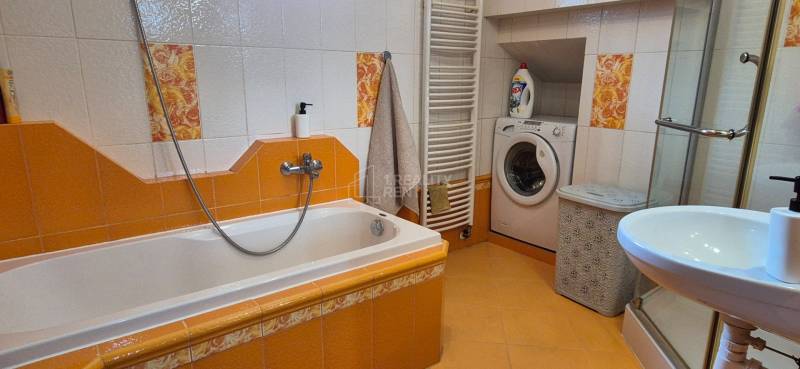 Ein Badezimmer in einem Einfamilienhaus mit einer Badewanne, einem Waschbecken, einer Waschmaschine und gelben Fliesen.