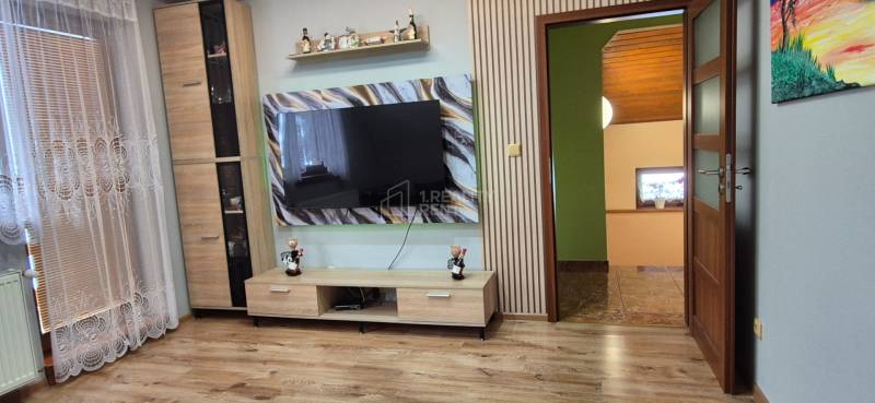 Wohnzimmer in einem Einfamilienhaus mit Holzdekorboden und einem großen Fernseher an der Wand.