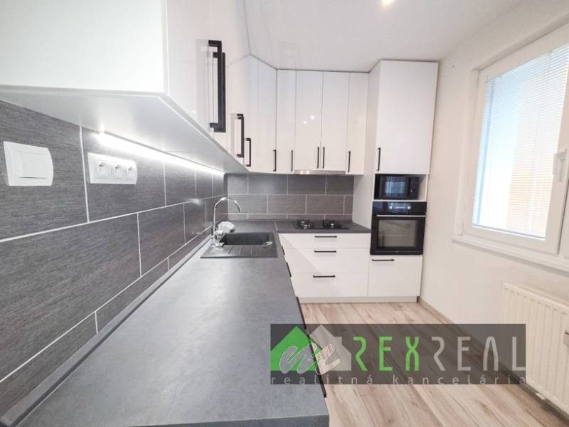 Küche in einer 3-Zimmer-Wohnung mit weißen Schränken, grauer Arbeitsplatte und Bodenbelag in Holzoptik.