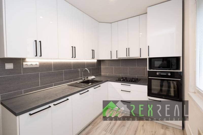 Küche in einer 3-Zimmer-Wohnung mit weißen Schränken und Geräten, Boden mit Holzdekor.