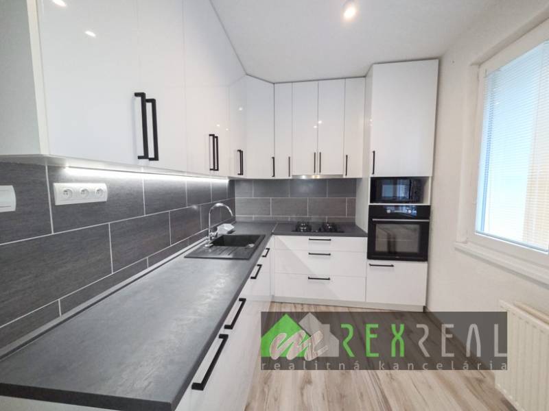 Küche in einer 3-Zimmer-Wohnung mit weißen Schränken und einem Boden in Holzoptik.