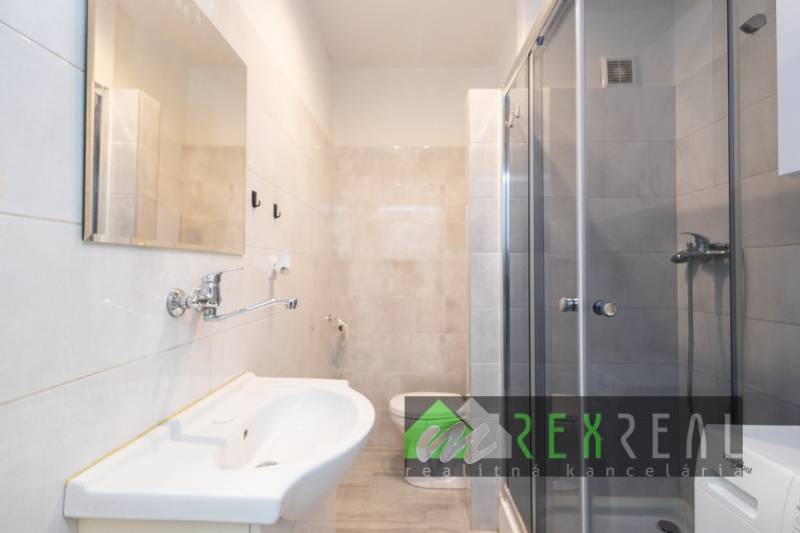 Badezimmer in einer 3-Zimmer-Wohnung mit Duschkabine, Waschbecken und hellen Fliesen.