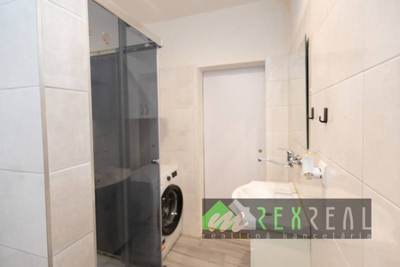 Badezimmer in einer 3-Zimmer-Wohnung mit Duschkabine und Waschmaschine, Fliesen an den Wänden.