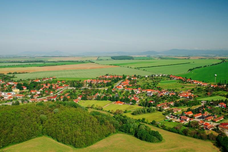 Luftaufnahme von Nemčiňany, umgeben von landwirtschaftlichen und forstwirtschaftlichen Flächen in einer grünen Landschaft.