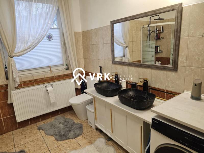 Ein Badezimmer in einem Einfamilienhaus mit Doppelwaschbecken, Badewanne und Waschmaschine auf Fliesen.