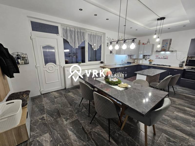 Essbereich mit Steintisch, grauen Stühlen und Hängelampen in einem Einfamilienhaus.