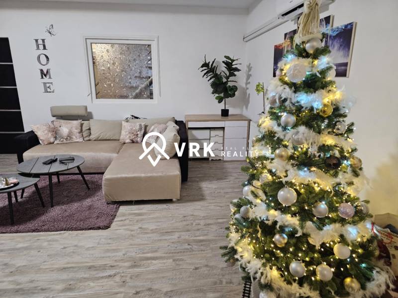 In einem Einfamilienhaus mit einem Boden in Holzoptik steht ein geschmückter Weihnachtsbaum und ein Sofa.