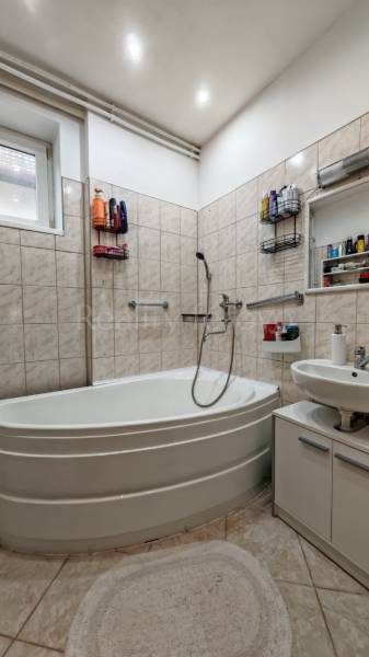 Badezimmer im Einfamilienhaus mit Eckbadewanne, Waschbecken und weißen Fliesen.