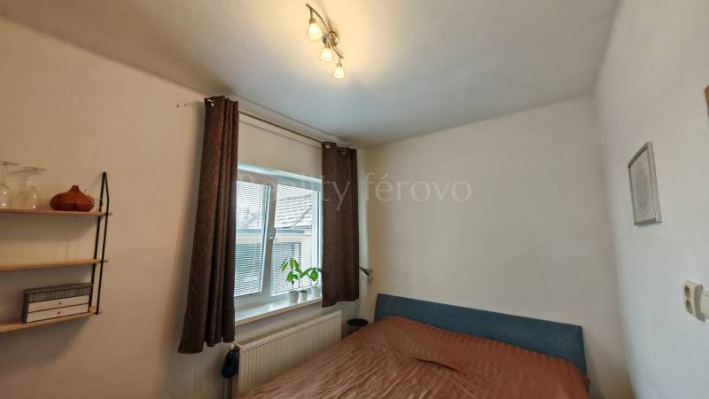 Schlafzimmer im Einfamilienhaus, mit Bett, Regalen und Fenster mit dekorativer Pflanze.