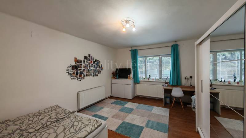 Ein Zimmer in einem Einfamilienhaus mit einem Schreibtisch, einem Bett, Fotos an der Wand und einem Boden in Holzoptik.