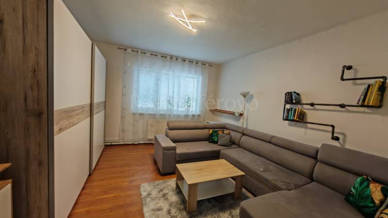 Ein Wohnzimmer in einem Einfamilienhaus mit einem Sofa, einem Bücherregal und einem Boden mit Holzdekor.