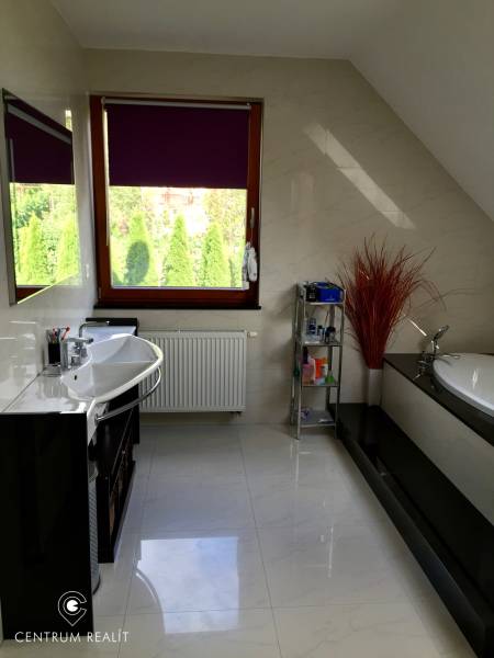 Ein Badezimmer in einem Einfamilienhaus mit einer Badewanne, einem Waschbecken, einem Regal und einem Fenster mit einer lila Jalousie.