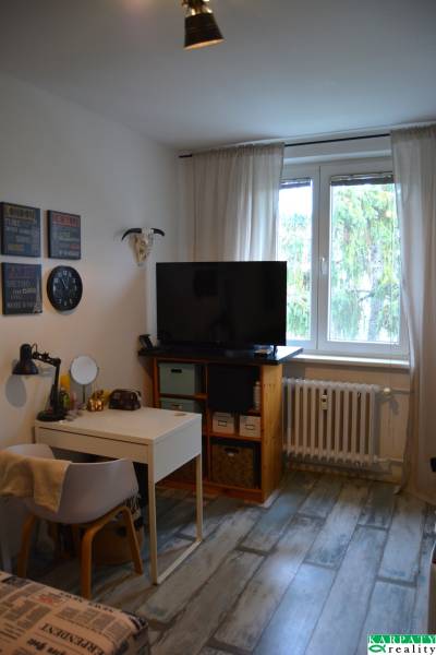 Wohnzimmer in einer 3-Zimmer-Wohnung mit Holzdekorboden, Fernseher und Schreibtisch.