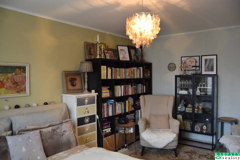 Ein Zimmer in einer 3-Zimmer-Wohnung mit einem Sessel, einem Bücherregal, Kronleuchtern und Dekorationen an den Wänden.