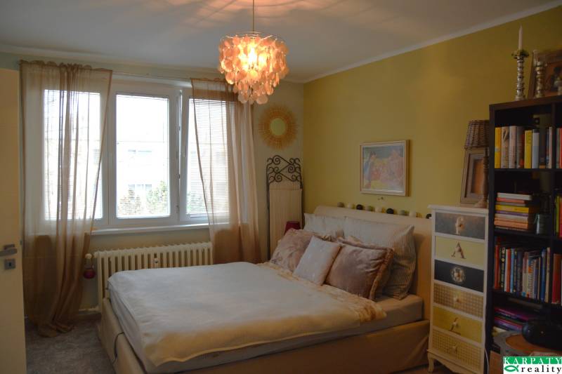 Gemütliches Schlafzimmer mit Vorhängen und Bücherregal in einer 3-Zimmer-Wohnung, die Atmosphäre wird durch einen interessanten Kronleuchter ergänzt.