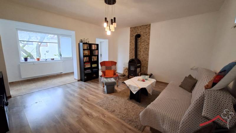 Ein Zimmer in einem Einfamilienhaus mit einem Kaminofen, einem Sofa, einem Bücherregal und einem Boden mit Holzdekor.