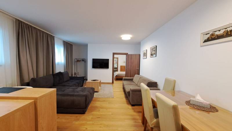 Wohnzimmer mit Sofa und Fernseher, neben dem Esstisch, Boden mit Holzdekor.