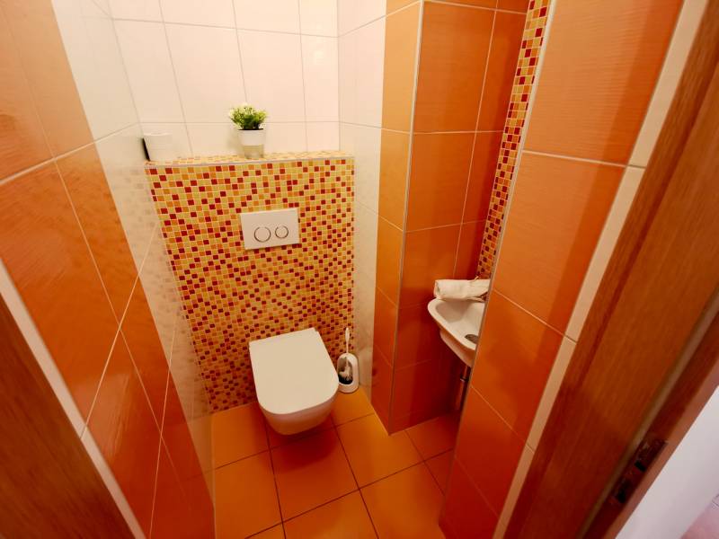 Toilette in einer 4-Zimmer-Wohnung mit orangefarbenen Fliesen und Mosaik, kleines Waschbecken in der Ecke.